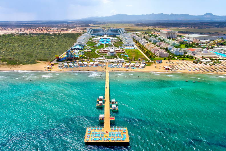 Długi pomost prowadzi przez turkusowe morze do luksusowego kurortu z plażą (widok z lotu ptaka).