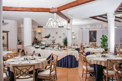 Restauracja z okrągłymi stołami, bufetem i drewnianym sufitem.