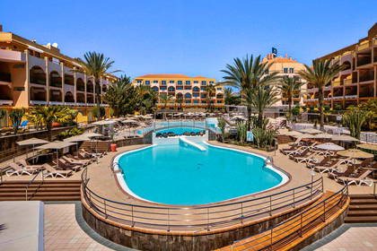 Kompleks hotelowy z basenem otoczonym palmami.