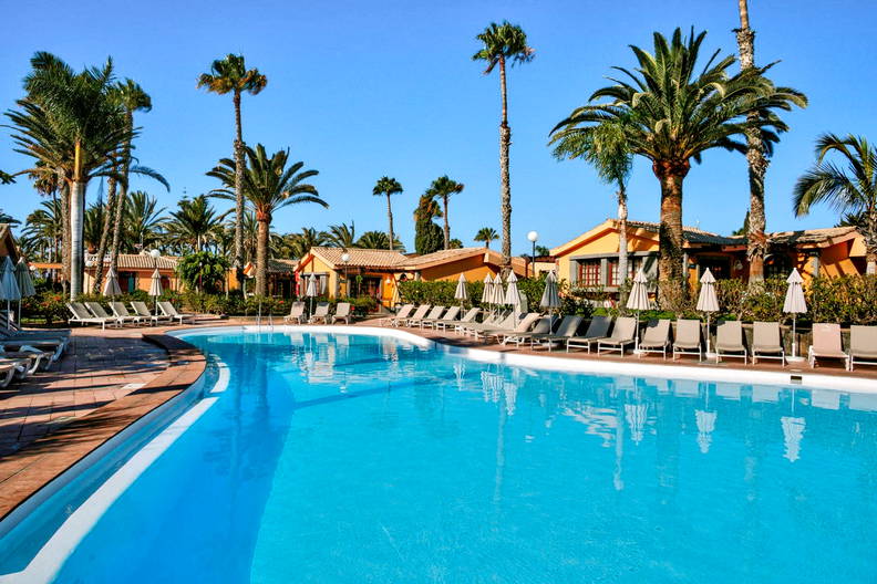 Turkusowy basen z palmami i leżakami.