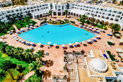 Hotel z dużym basenem, palmami i leżakami, widok z góry.