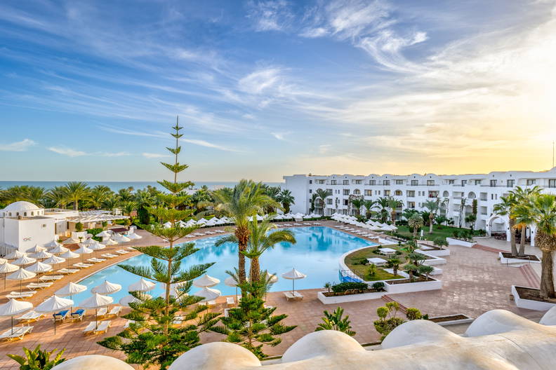 Basen w tropikalnym kurorcie z palmami i białymi parasolami.