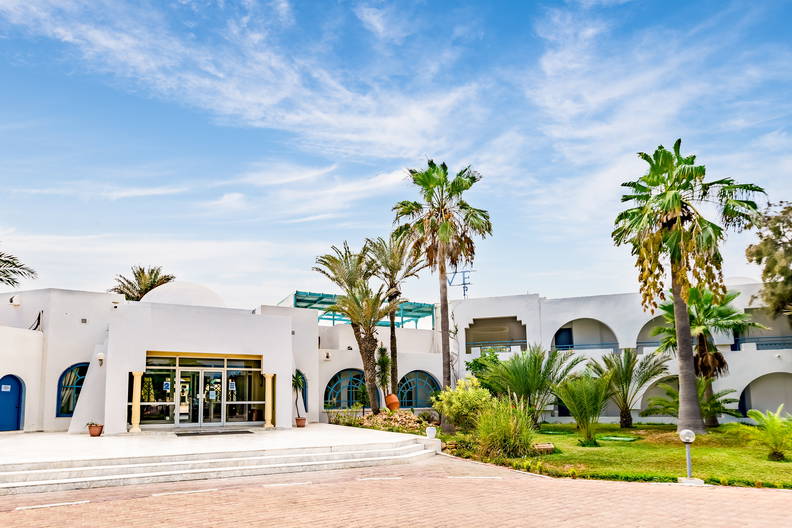 Biały budynek hotelu z palmami na tle błękitnego nieba.