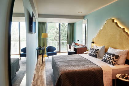 Pokój hotelowy z łóżkiem, fotelem i widokiem na zieleń.