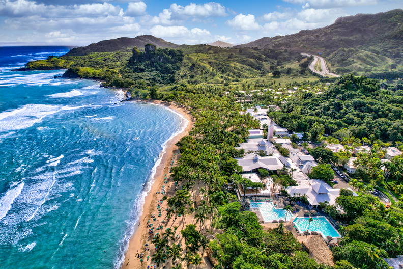 Plaża, hotel i góry w słoneczny dzień z lotu ptaka.