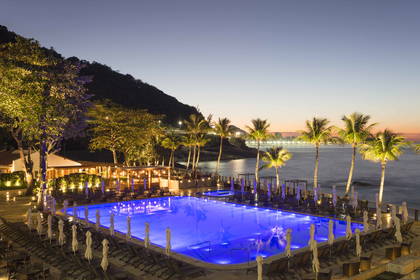 Nocny widok na hotelowy basen, palmy i ocean.