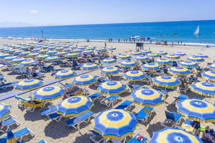 Plaża z lotu ptaka. Widoczne niebiesko-żółte parasole i leżaki.
