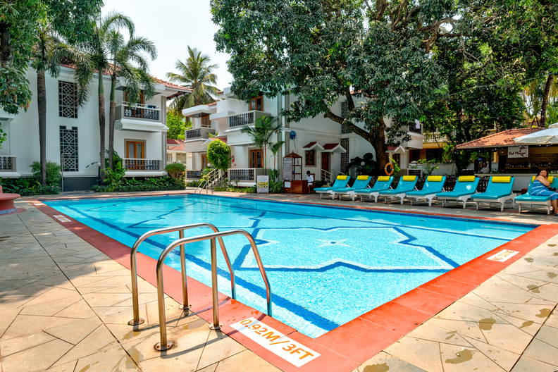 Basen hotelowy z leżakami i białymi budynkami w tle.