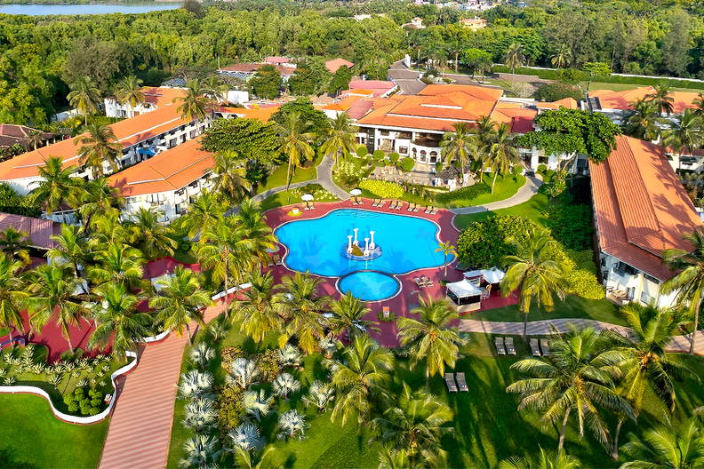 Widok z lotu ptaka na luksusowy kurort. Na zdjęciu basen, palmy i budynki z czerwonymi dachami.