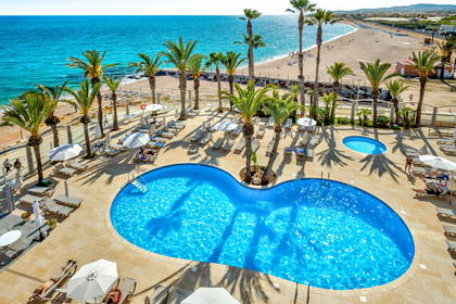 Hotel z basenem, leżakami i palmami. W tle plaża i ocean (widok z góry).