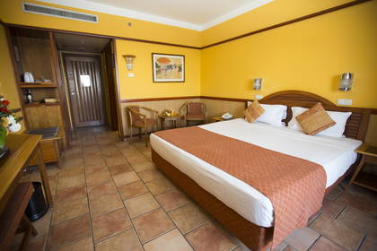 Żółty pokój hotelowy z dużym łóżkiem i terakotową podłogą.