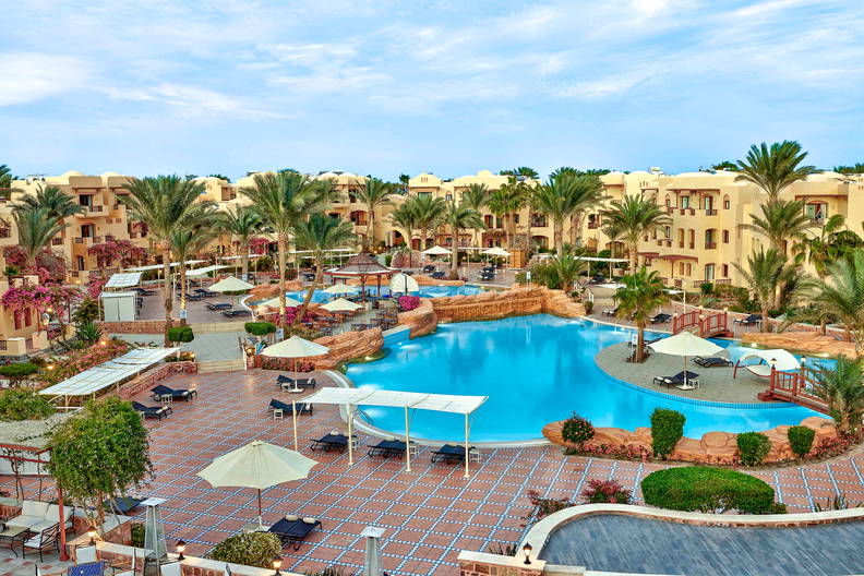 Kompleks wypoczynkowy z basenami, palmami i budynkami w tle.