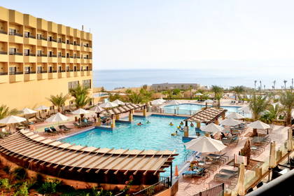 Hotel z basenem, leżakami i parasolami. W tle widok na ocean.