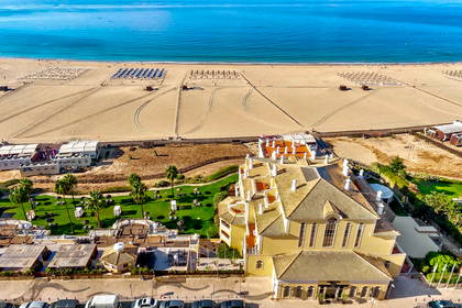 Widok z góry na plażę, hotel z zielenią i ocean.