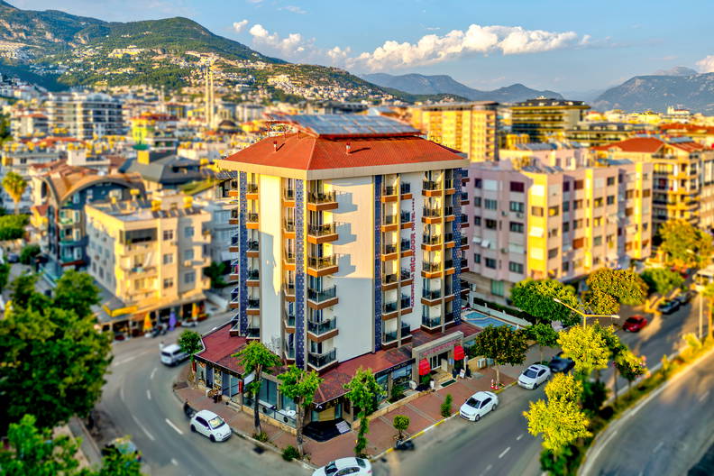 Hotel na rogu ulicy, widziany z góry. W tle gęsta zabudowa miasta i góry.