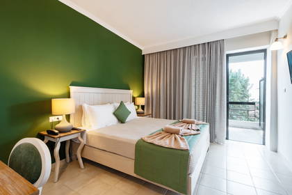 Jasny pokój hotelowy z łóżkiem, balkonem i ścianą z roślin.