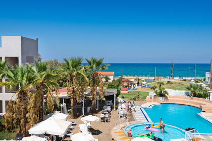 Hotel z basenem, palmami i plażą w tle.