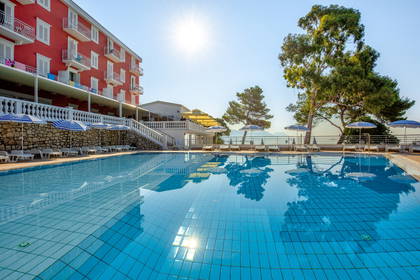 Hotel z basenem i leżakami w słoneczny dzień.