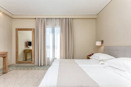Pokój hotelowy z dwoma łóżkami, lustrem i zasłonami w oknach.
