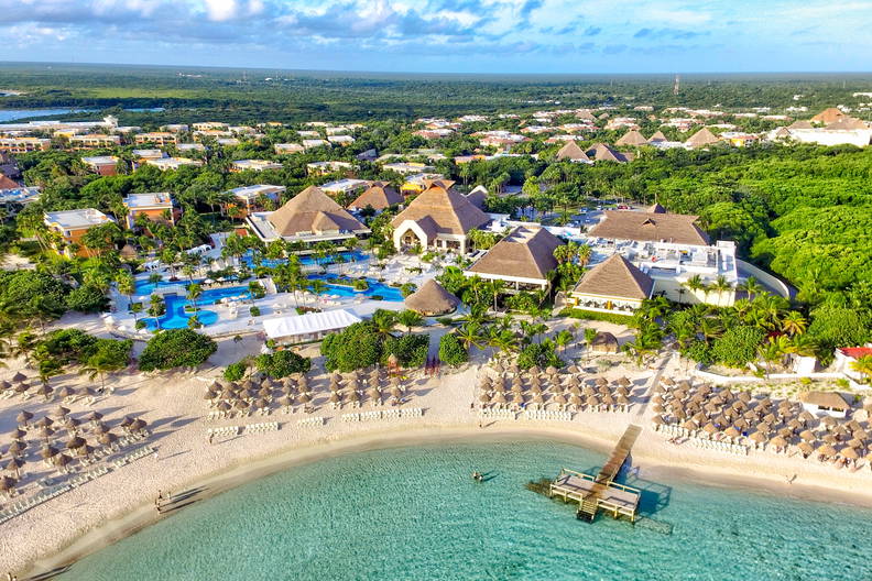 Kurort z lotu ptaka: plaża, baseny i budynki kryte strzechą.