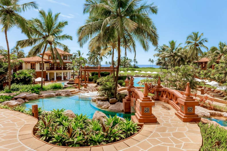 Kompleks hotelowy z basenami, palmami i małym mostkiem.