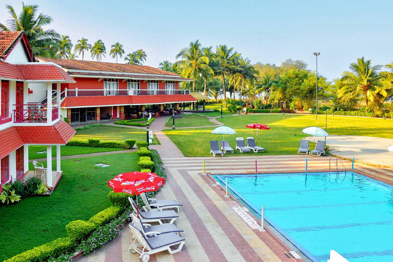 Kompleks wypoczynkowy z basenem, leżakami i trawnikiem.