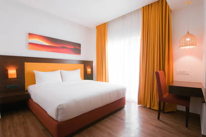 Pokój hotelowy z łóżkiem, biurkiem i pomarańczowymi zasłonami.