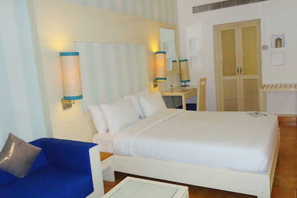 Pokój hotelowy z białym łóżkiem, biurkiem i niebieską kanapą.