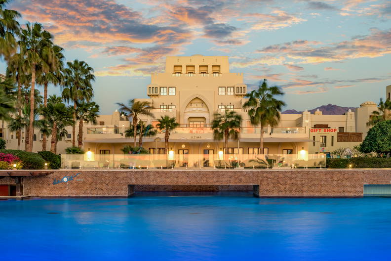 Hotel w tropikalnym kurorcie z basenem otoczonym palmami.