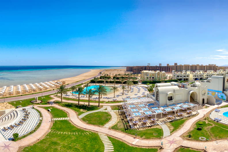 Hotel z basenami i plażą nad morzem w słoneczny dzień.