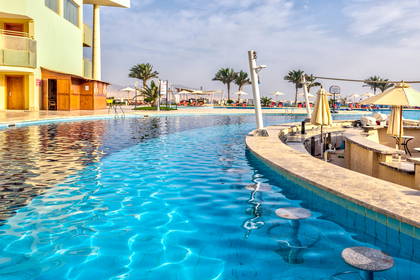 Basen hotelowy z barem wodnym i palmami.