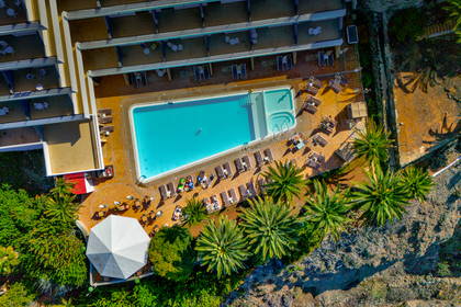 Hotel z basenem, leżakami i palmami, widok z góry.