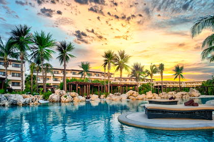 Resort z basenem i palmami w promieniach zachodzącego słońca.