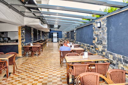 Zadaszona restauracja na świeżym powietrzu ze stolikami i krzesłami.