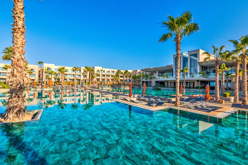 Resort z basenem i palmami. W tle budynki.