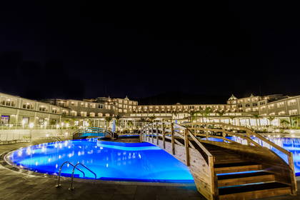 Oświetlony basen z drewnianym mostkiem w hotelu nocą.
