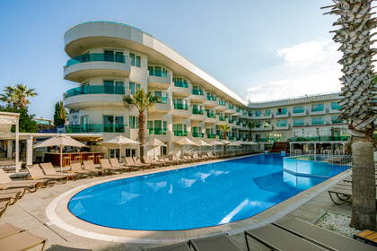 Nowoczesny hotel z dużym, błękitnym basenem otoczonym leżakami i palmami.