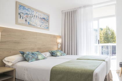 Pokój hotelowy z dwoma łóżkami i oknem. Na ścianie wisi obraz.
