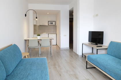 Wnętrze apartamentu. Dwie niebieskie kanapy, stół i aneks kuchenny.