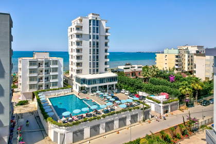Biały hotel z basenem widziany z góry, w tle błękitne morze.