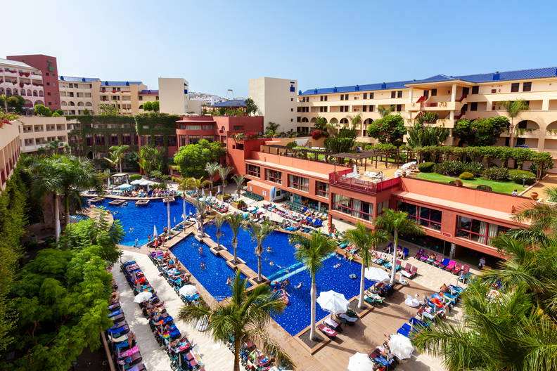 Hotelowy basen otoczony budynkami i palmami, widok z góry.