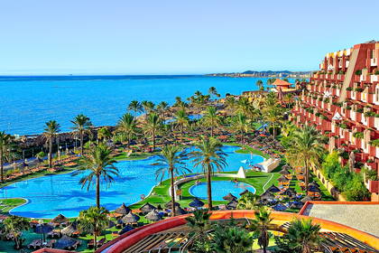 Hotel z basenami i palmami. W tle widok na morze.
