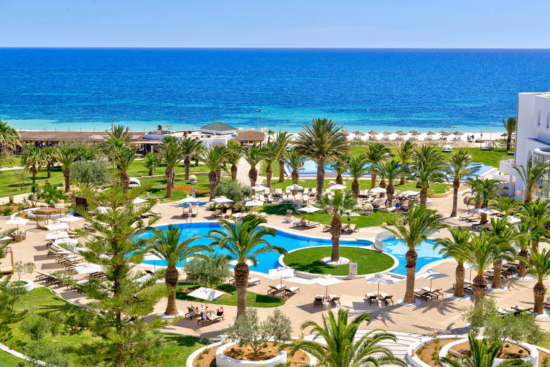 Hotel z basenem i palmami. W tle widoczny ocean (widok z góry).