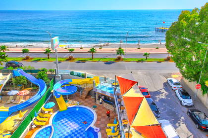 Widok z góry na hotel z basenem, leżakami, zjeżdżalniami, plażą i morzem.