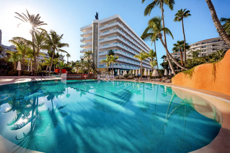 Basen w hotelu otoczony palmami w słoneczny dzień.