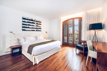 Jasny pokój hotelowy z drewnianą podłogą i balkonem.