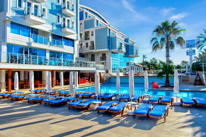 Hotel z basenem, leżakami i palmą w słoneczny dzień.