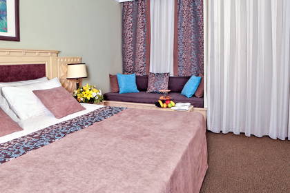 Pokój hotelowy z łóżkiem, kwiatami i sofą pod oknem.