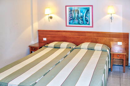 Pokój hotelowy z dwoma łóżkami i szafkami nocnymi.