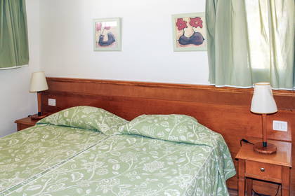 Pokój hotelowy z dwoma łóżkami, lampkami nocnymi i zielonymi zasłonami w oknach.